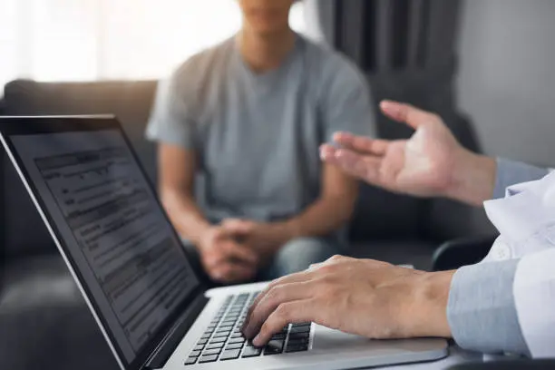 Doctor is using a laptop while typing the patient personal history record and giving advice about the patient home treatment.